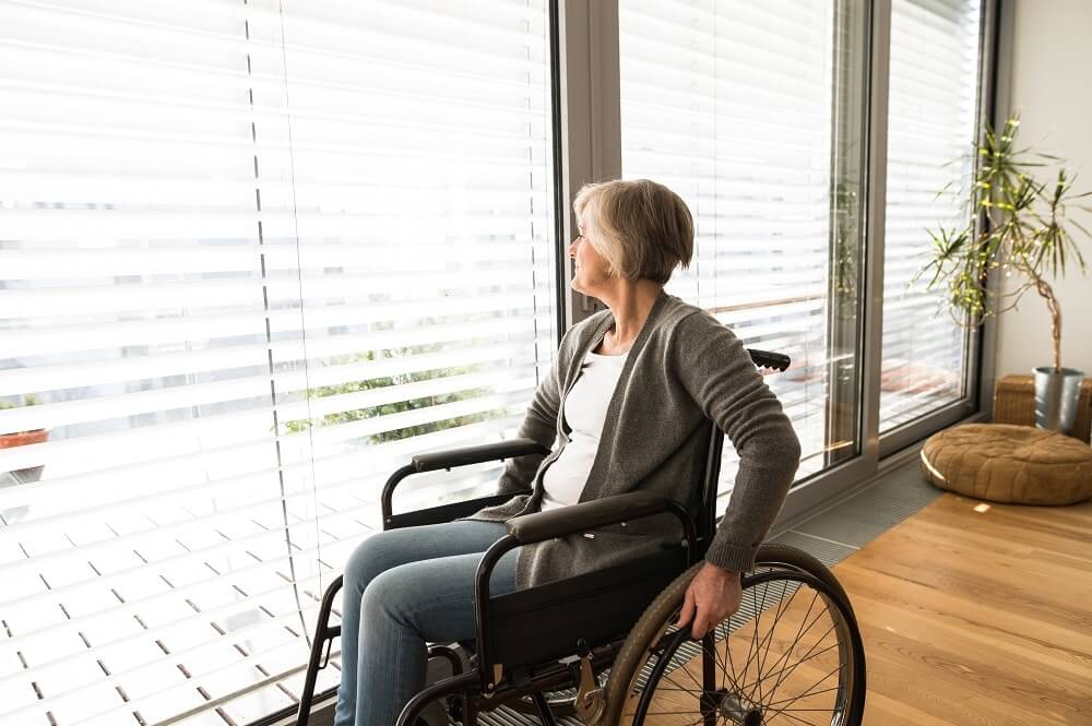 Ältere Frau im Rollstuhl blickt aus einem großen Fenster in einer hellen, barrierefreien Wohnung – Symbolbild für altersgerechtes Wohnen, Barrierefreiheit und selbstbestimmtes Leben im Alter.